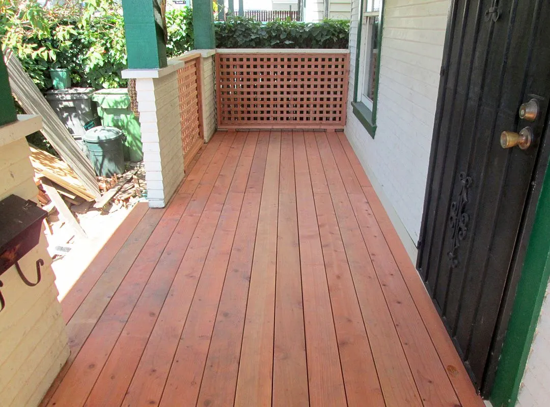 A porch with a wooden floor and a green door