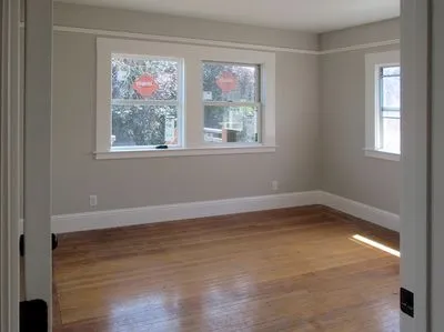 An empty room with hardwood floors and two windows.