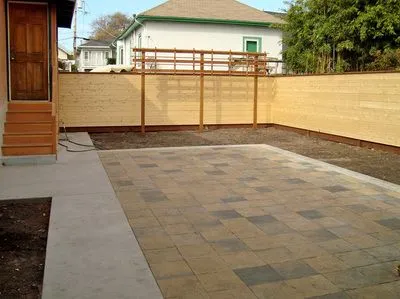 A backyard with a wooden fence and a brick walkway