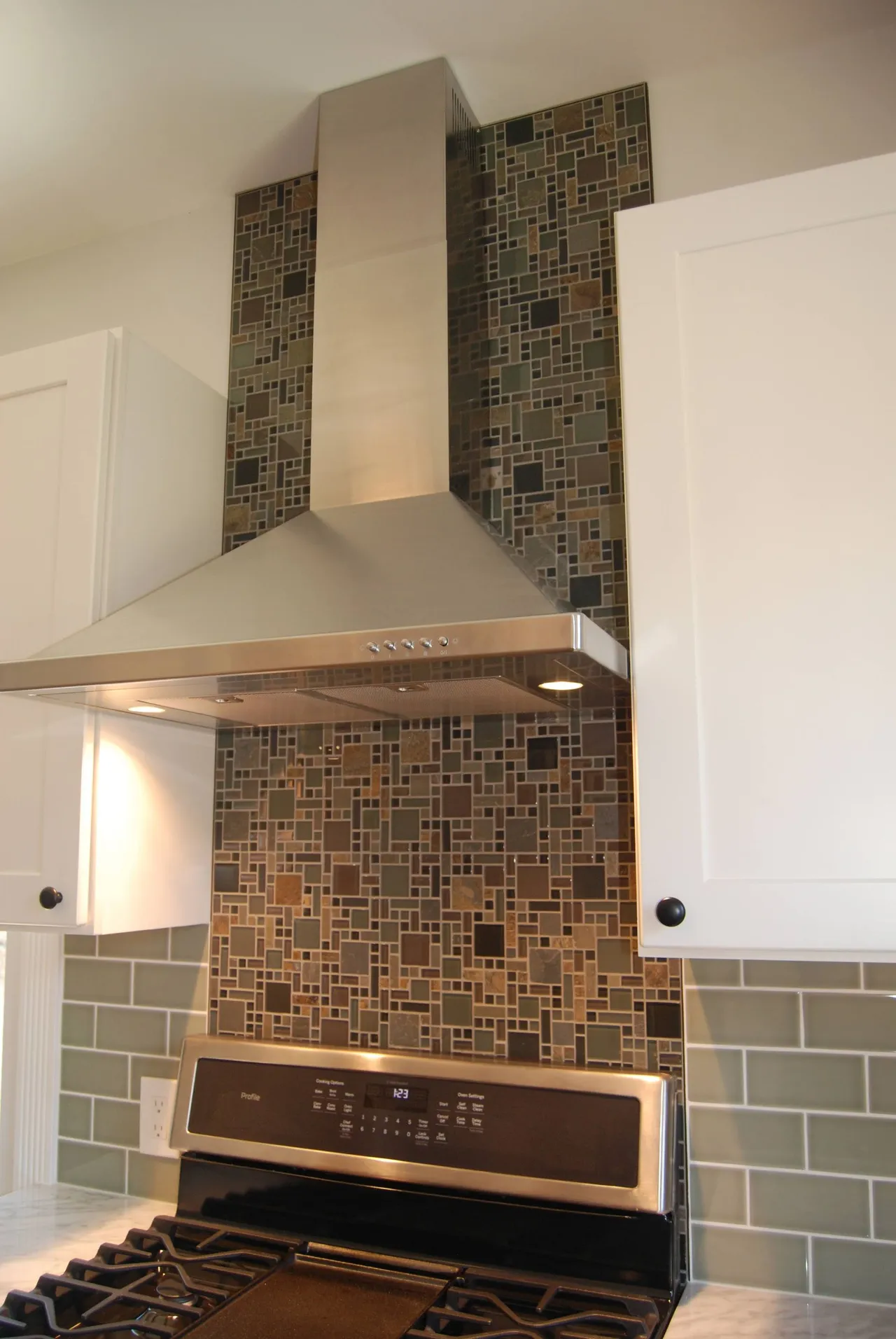 Modern kitchen stove with stainless range hood and mosaic tile backsplash