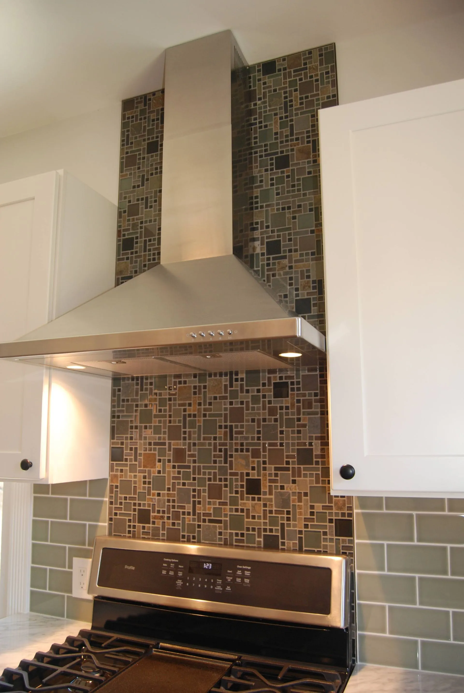 Modern kitchen stove with stainless range hood and mosaic tile backsplash