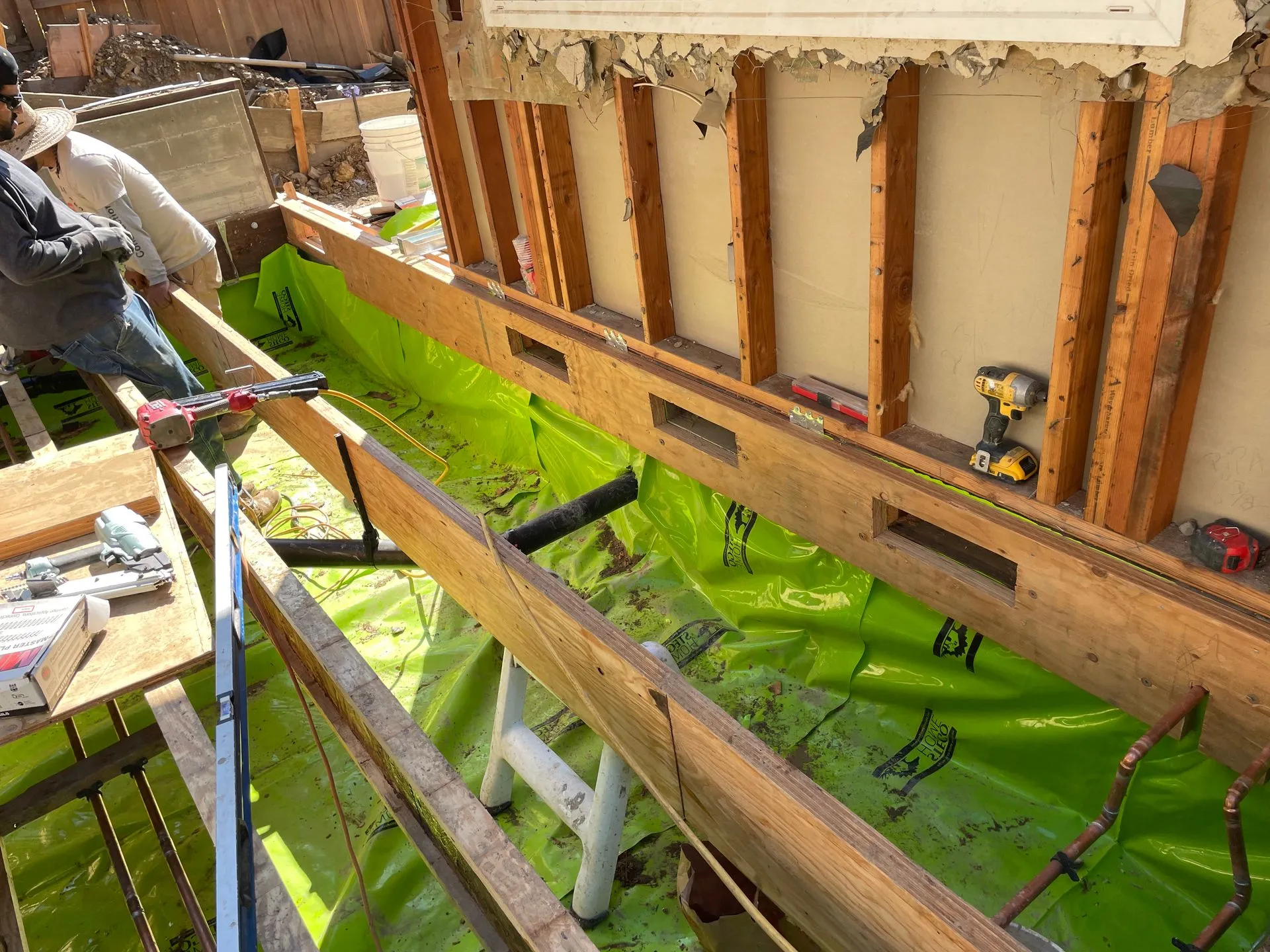 Workers installing bright green waterproofing on a house foundation during construction