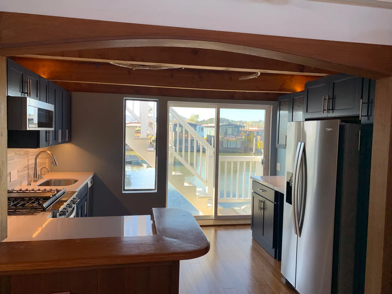 Modern kitchen with dark cabinets, stainless steel appliances, wood ceiling, and sliding glass door to a deck.