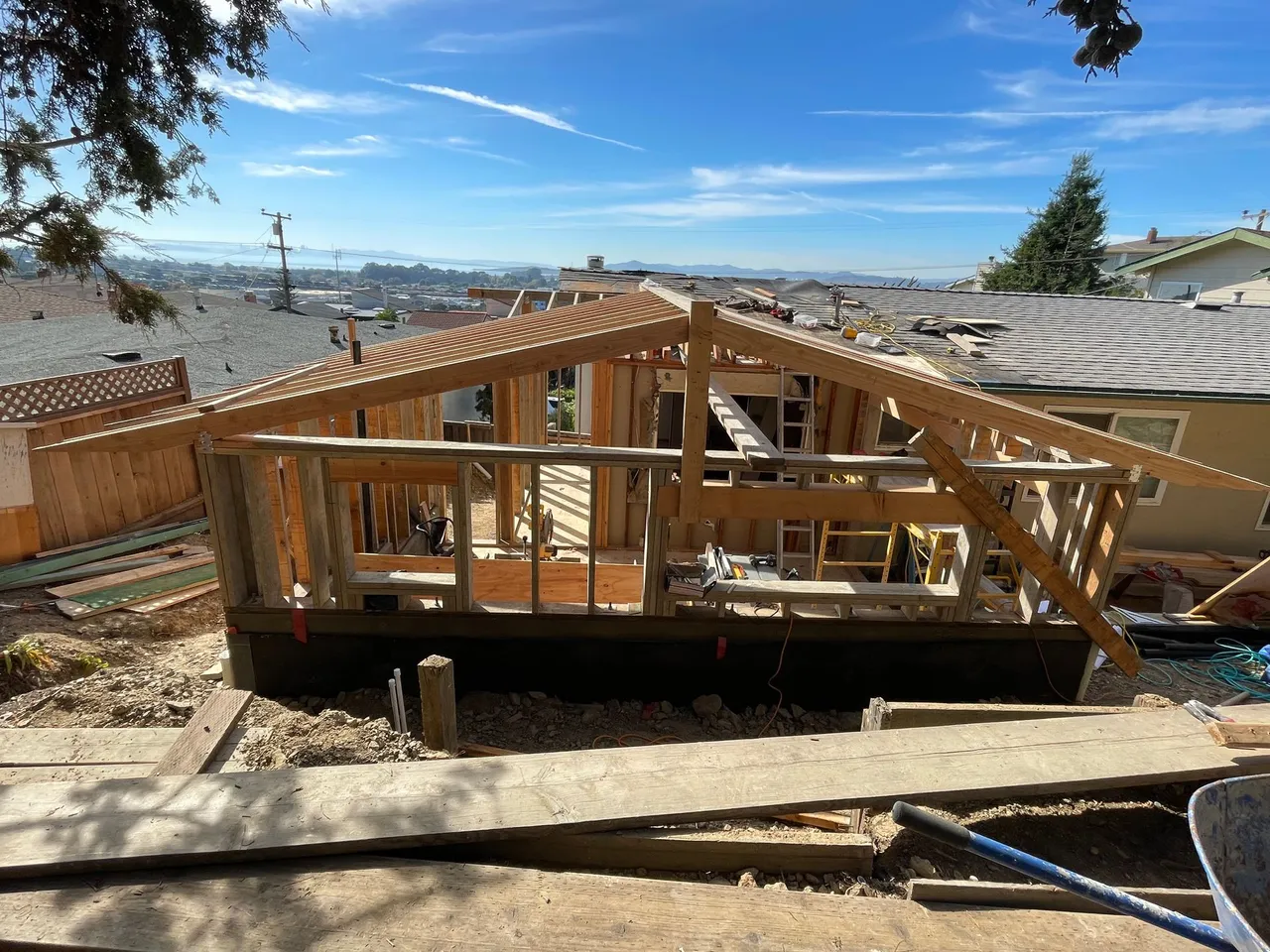 Wood-framed house under construction on a hillside with city views and a clear blue sky