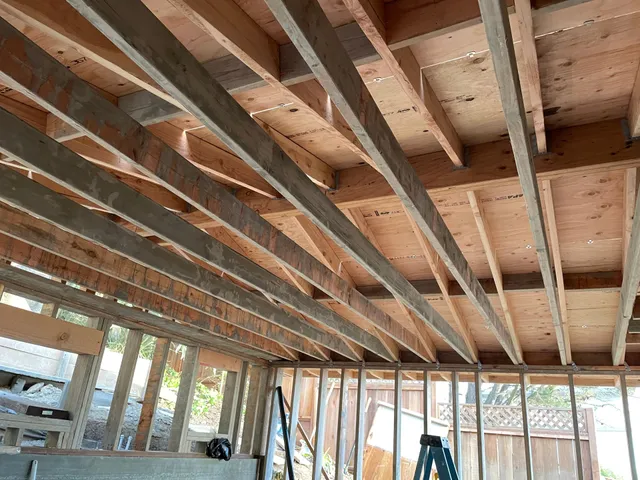 Exposed wooden ceiling joists and roof framing in an unfinished room under construction