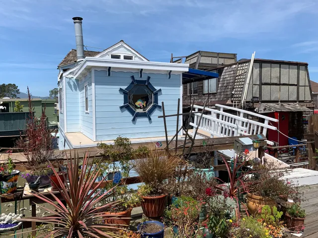 Light blue house with a star-shaped window, white ramp, and colorful potted garden in front