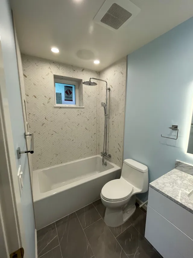 Small modern bathroom with bathtub, shower, toilet, and light blue walls