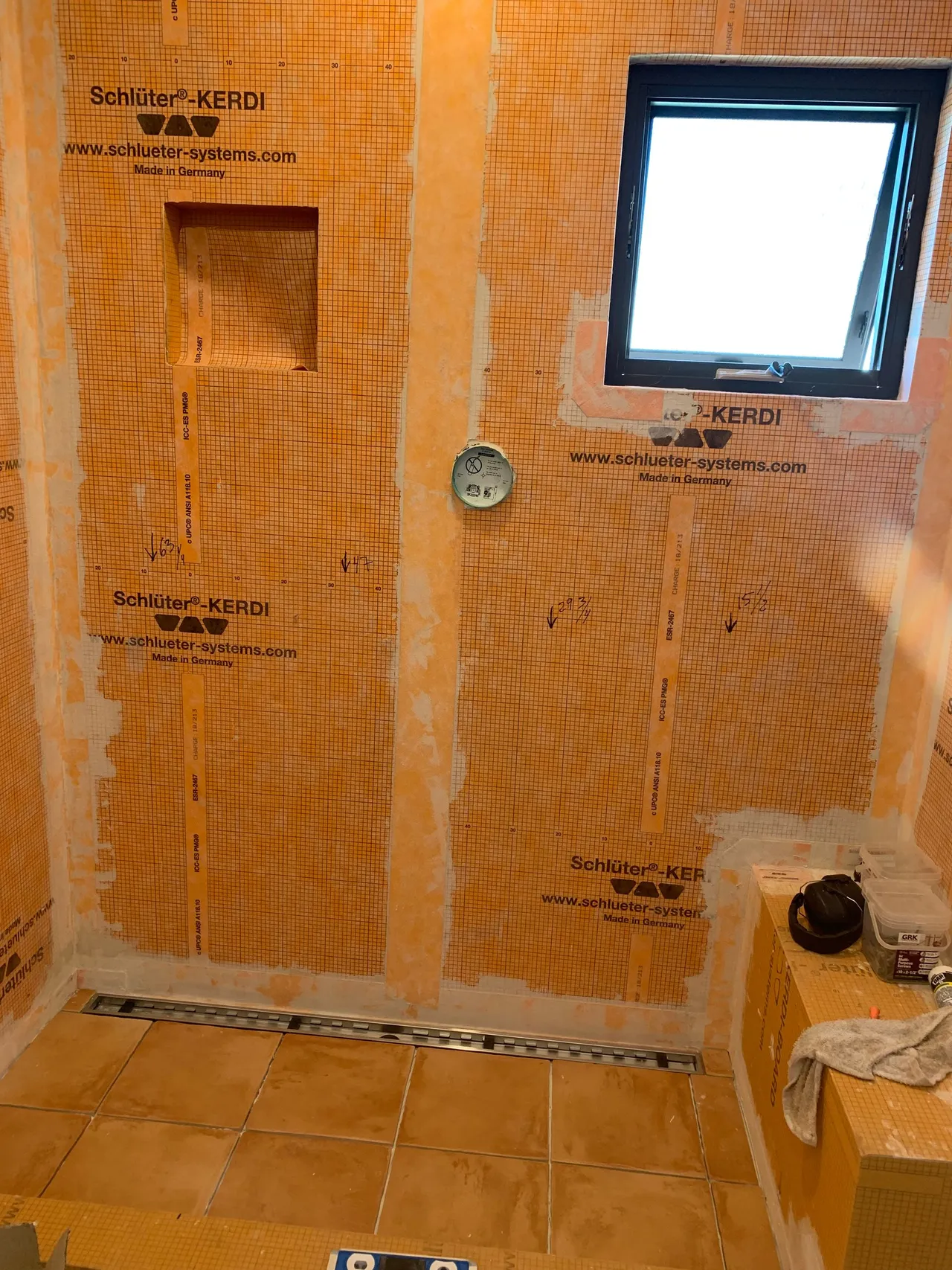 Orange waterproofed bathroom under renovation with tiled walls, a window, and exposed plumbing outlet
