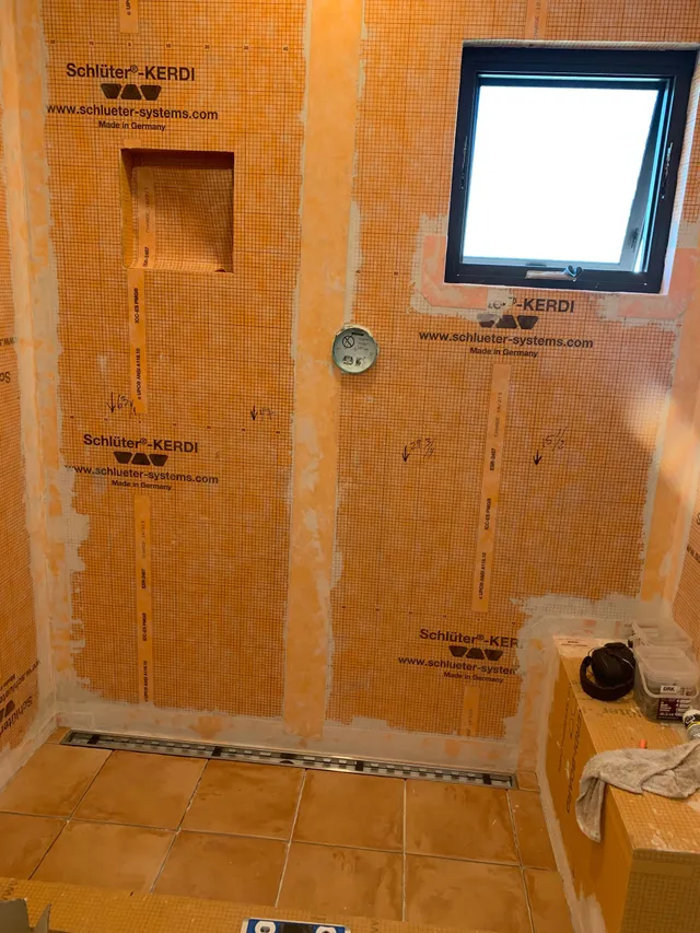 Orange waterproofed bathroom under renovation with tiled walls, a window, and exposed plumbing outlet