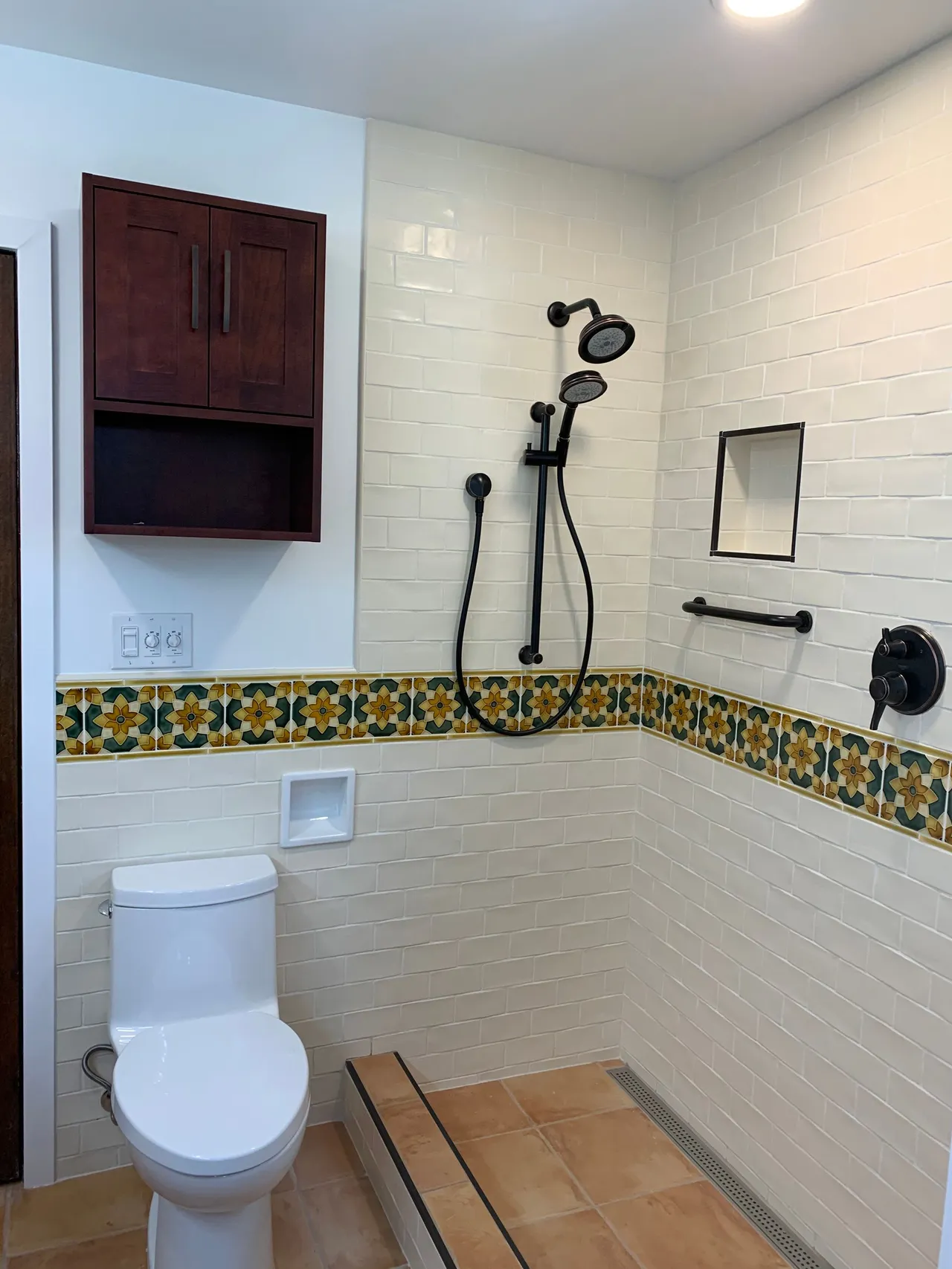 Accessible bathroom with toilet, wall-mounted shower, grab bar, and tiled bench area.