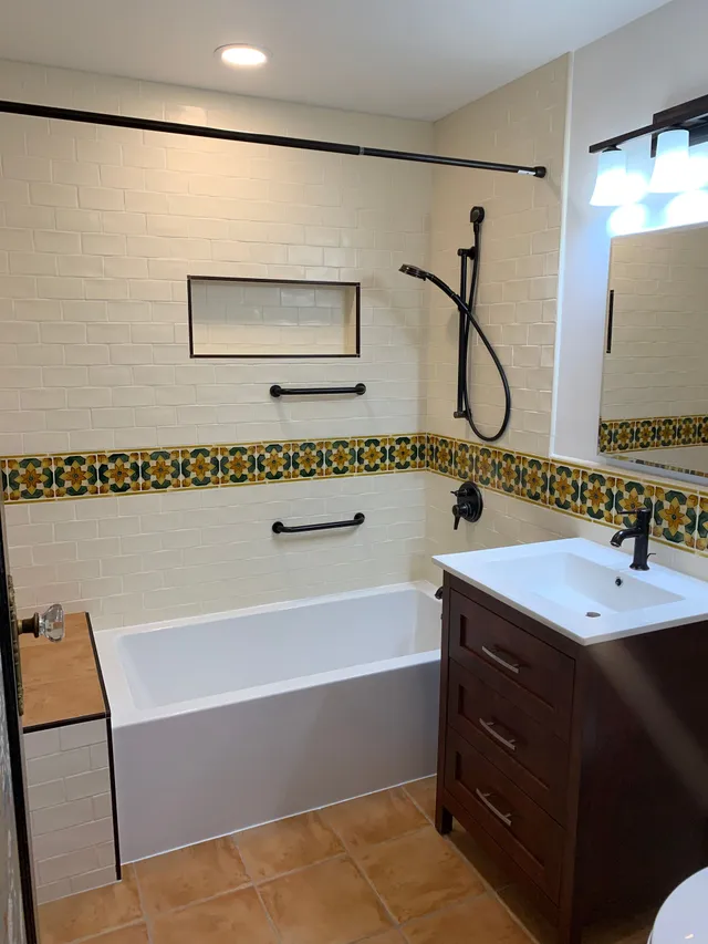 Bathroom with white tub, walk-in shower, floral tile border, and dark wood vanity.