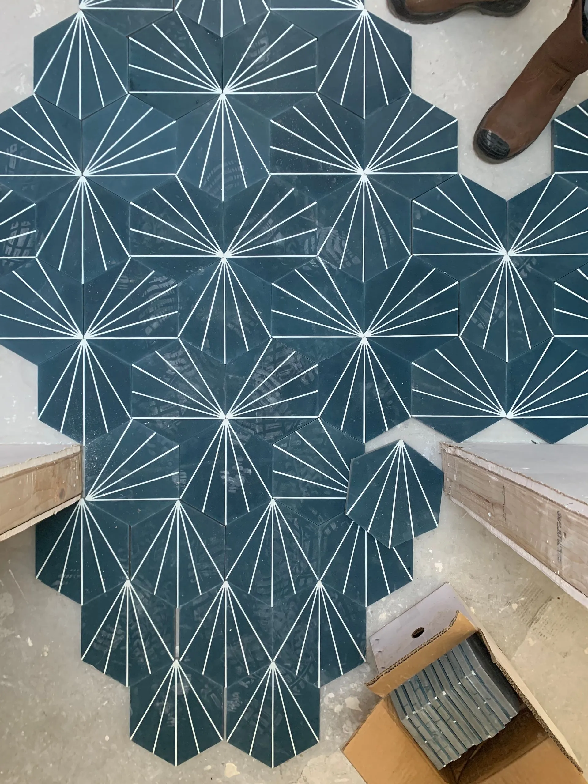 Blue geometric-patterned rug on a tiled floor, with a person’s shoes and a staircase visible nearby