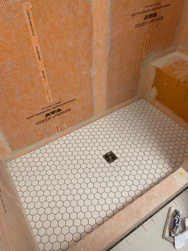 Small tiled shower floor with a central drain and orange waterproofing walls under construction