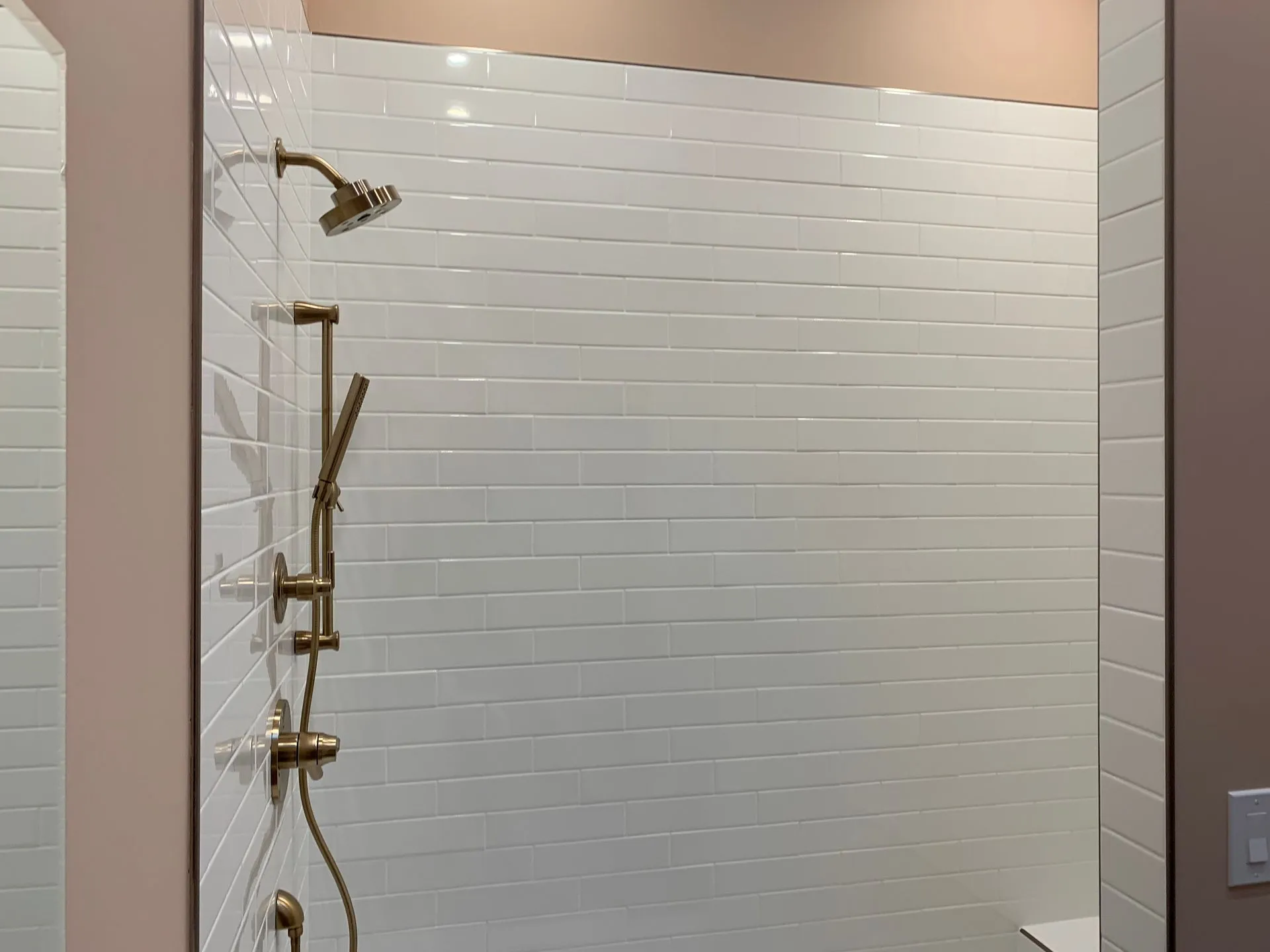 Empty shower stall with white tile walls and gold shower fixtures