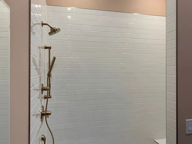 Empty shower stall with white tile walls and gold shower fixtures