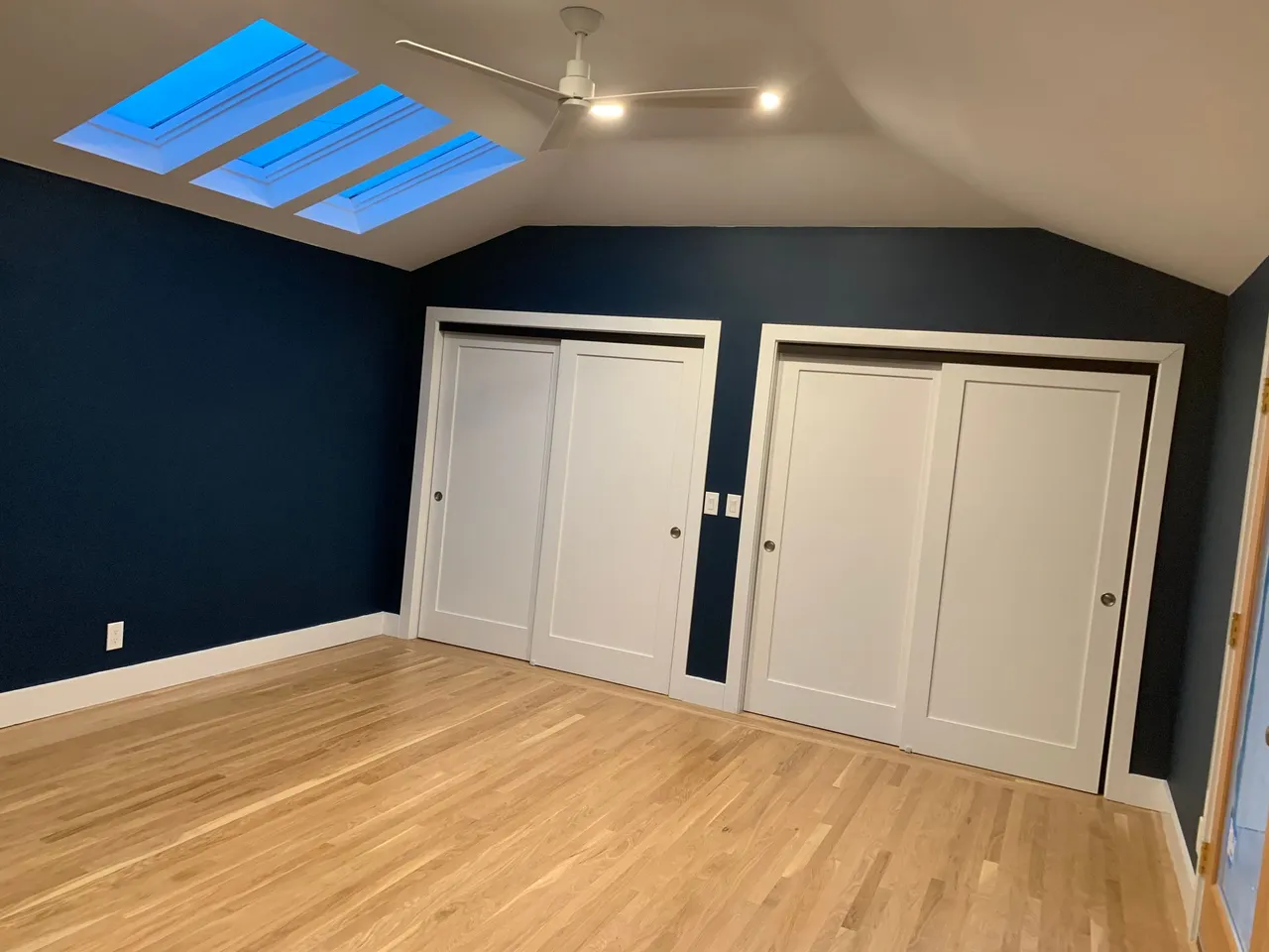 Empty attic-style room with dark blue walls, light wood floor, skylight, and double closet doors.
