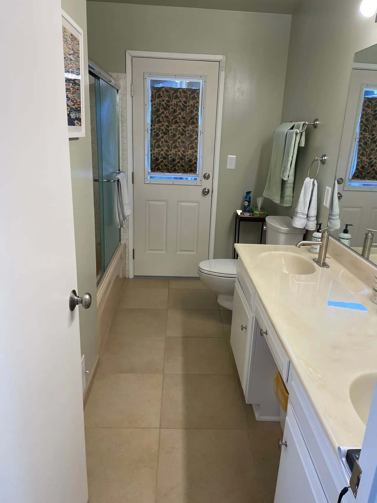 Narrow bathroom with beige tile, white vanity, toilet, and a door with a window at the end.