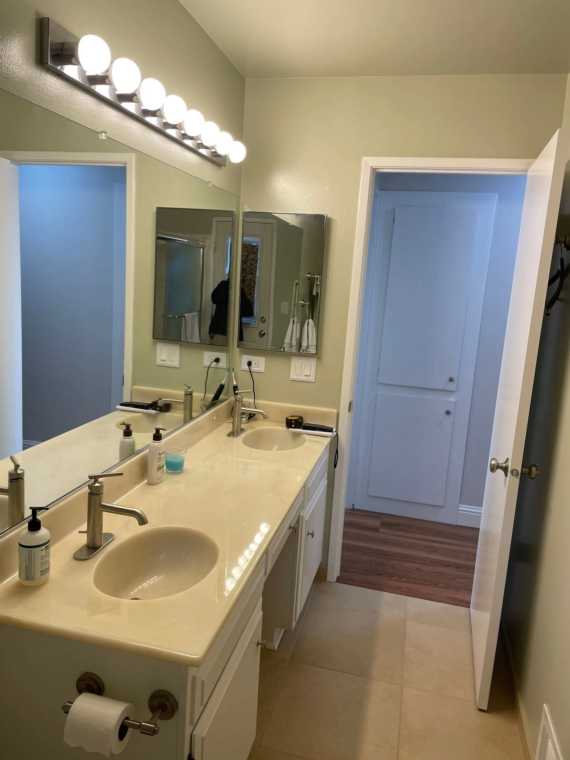 Bright bathroom vanity with double sinks, large mirror, and overhead lights beside a shower door