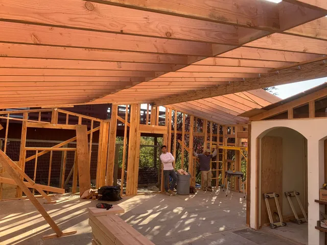 Partially built house interior with exposed wooden framing and a worker under construction.