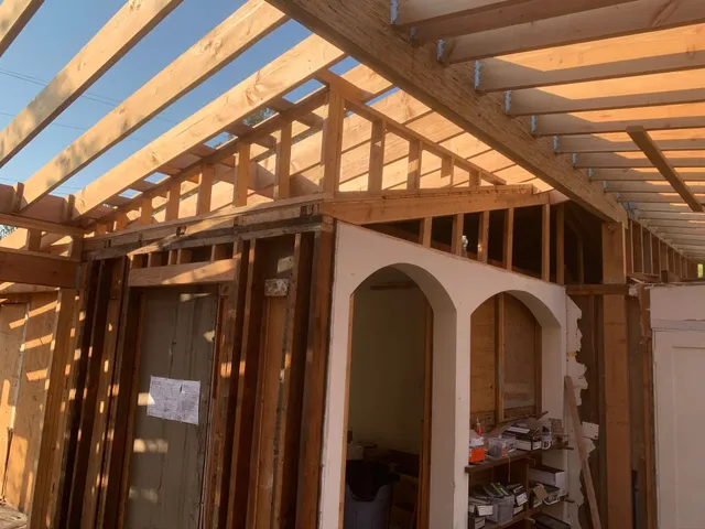 Partially built room with exposed wooden roof beams and white arched shelving under construction