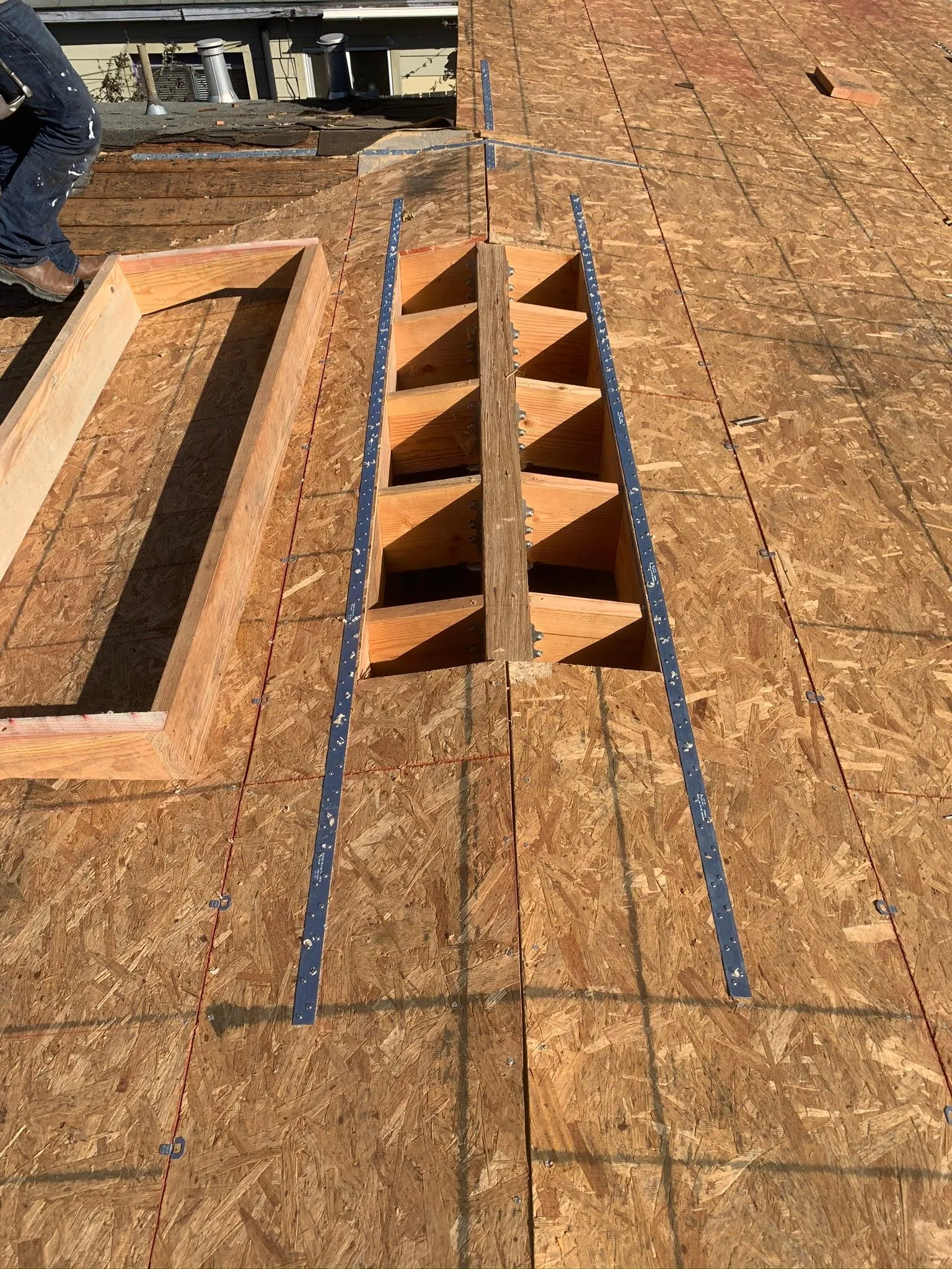 Construction site with wooden floor, rectangular opening, and a narrow orange stairwell framed by blue tape.