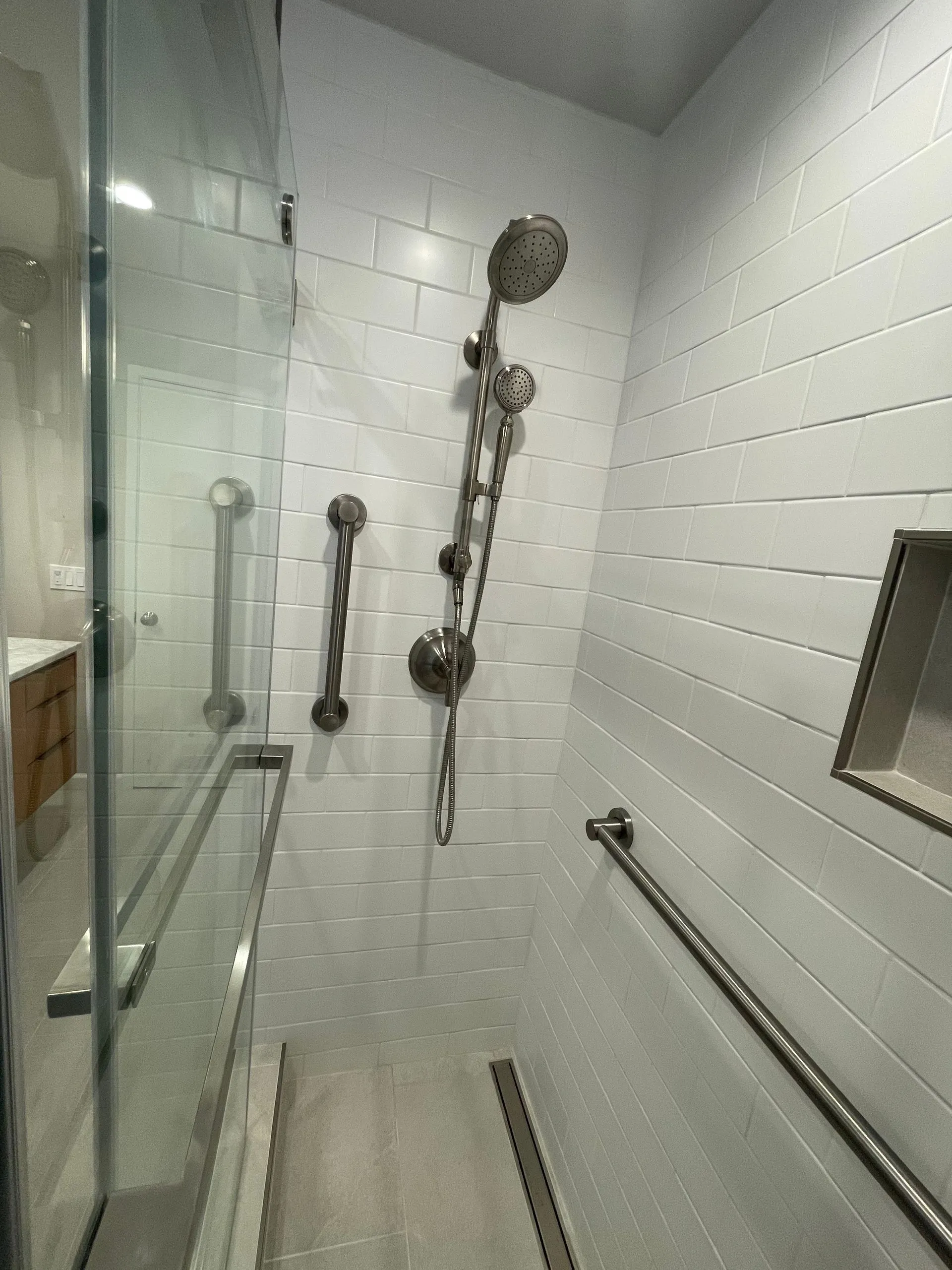 Small accessible shower with grab bars, bench, and handheld showerhead in a tiled bathroom
