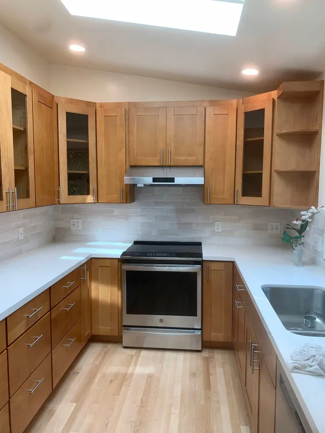 Small galley kitchen with wood cabinets, white countertops, stainless oven, and sink under skylights.