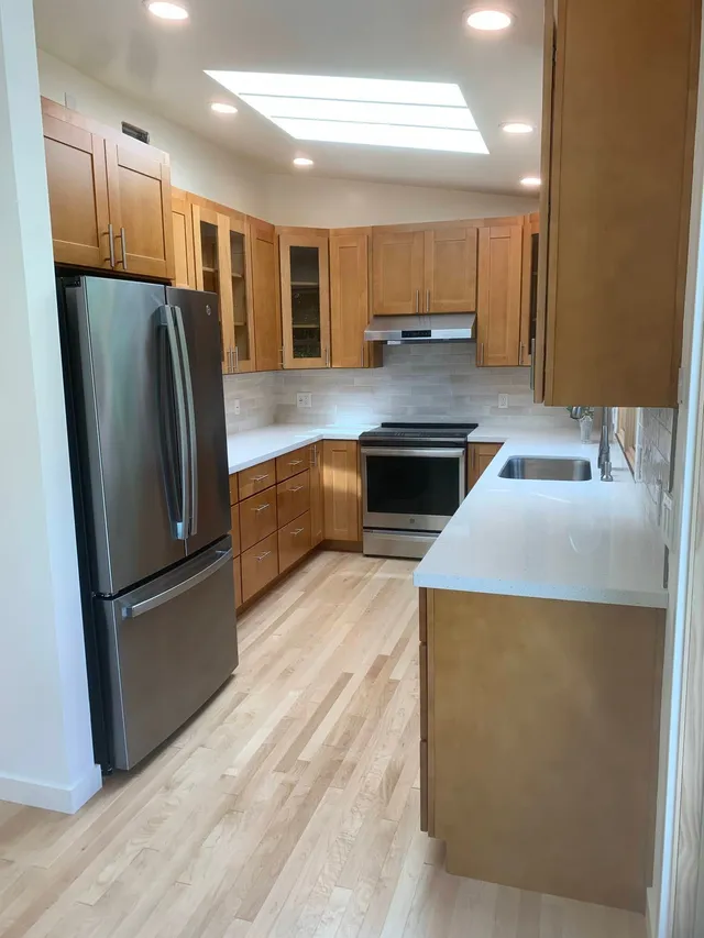 Modern kitchen with stainless steel appliances, light wood cabinets, and a white countertop under skylights