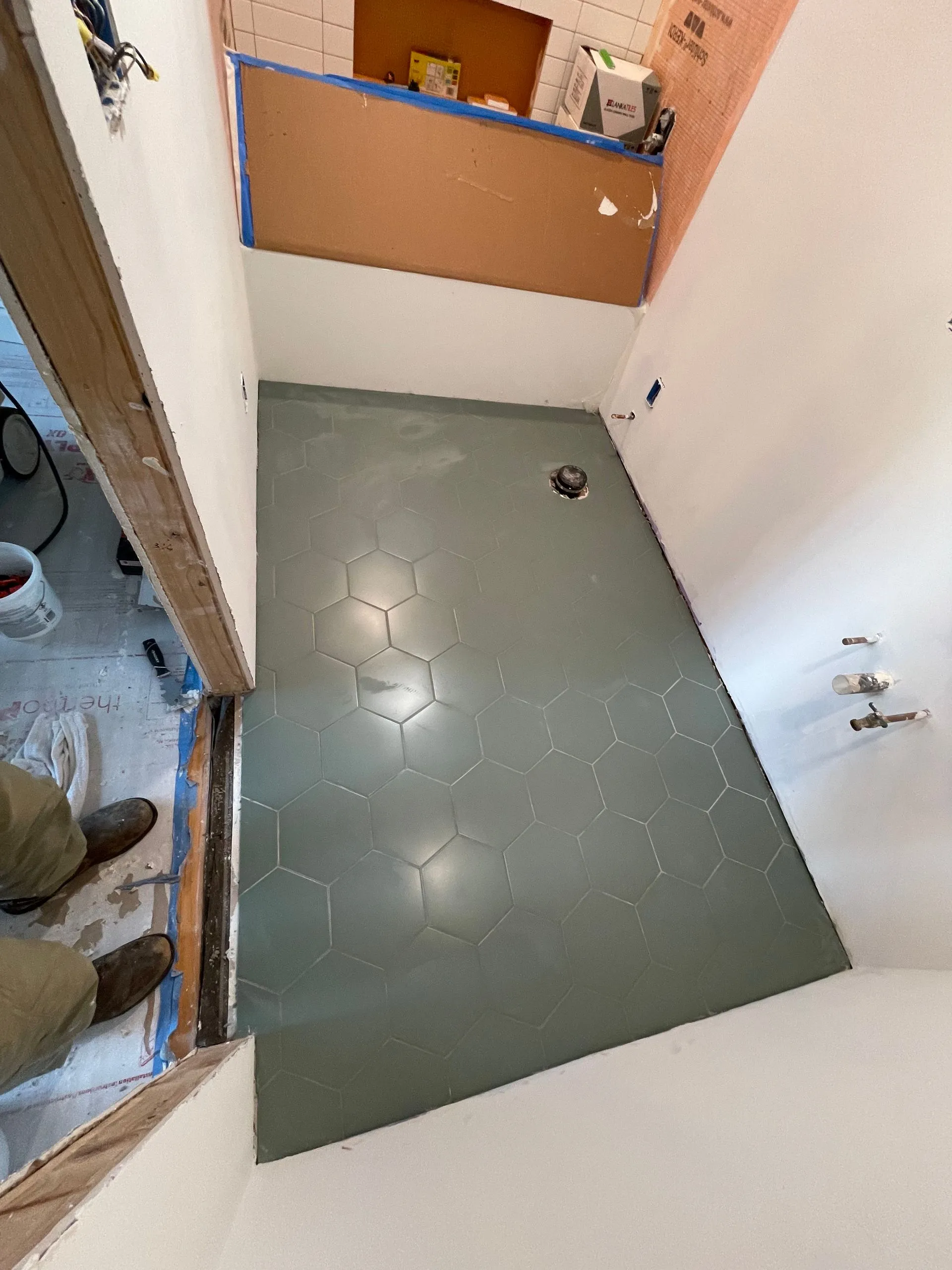Small bathroom with green tiled floor, white walls, and a wooden cabinet over the toilet area.