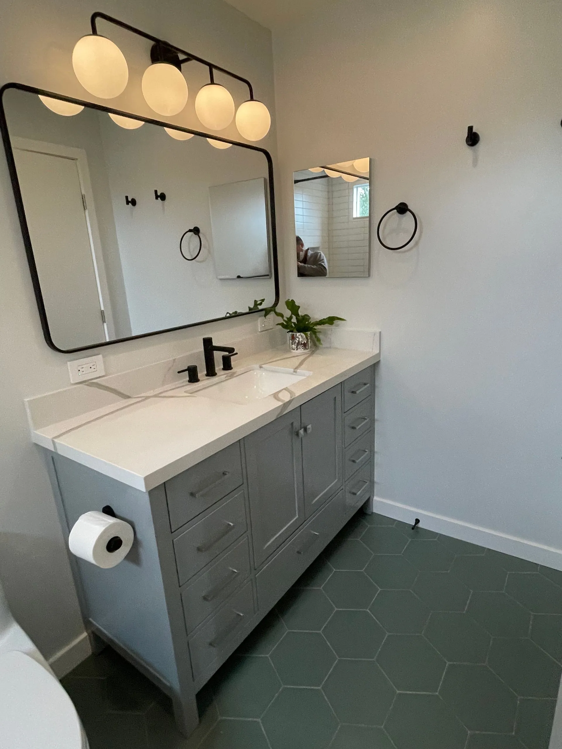 Modern bathroom vanity with large mirror, wall lights, gray cabinets, and green hex tile floor
