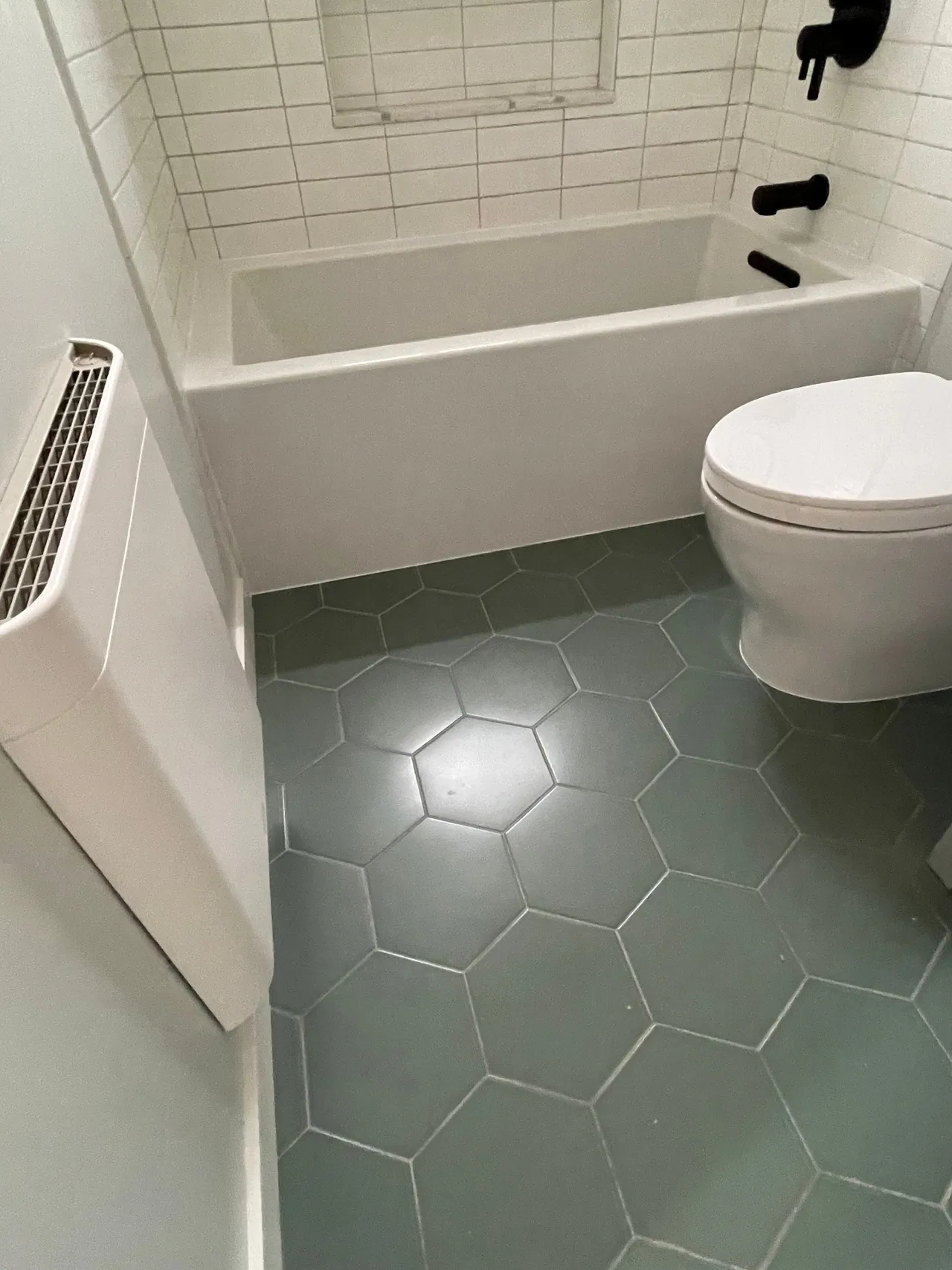 Small bathroom with white tub and toilet, green hex tile floor, and wall radiator.