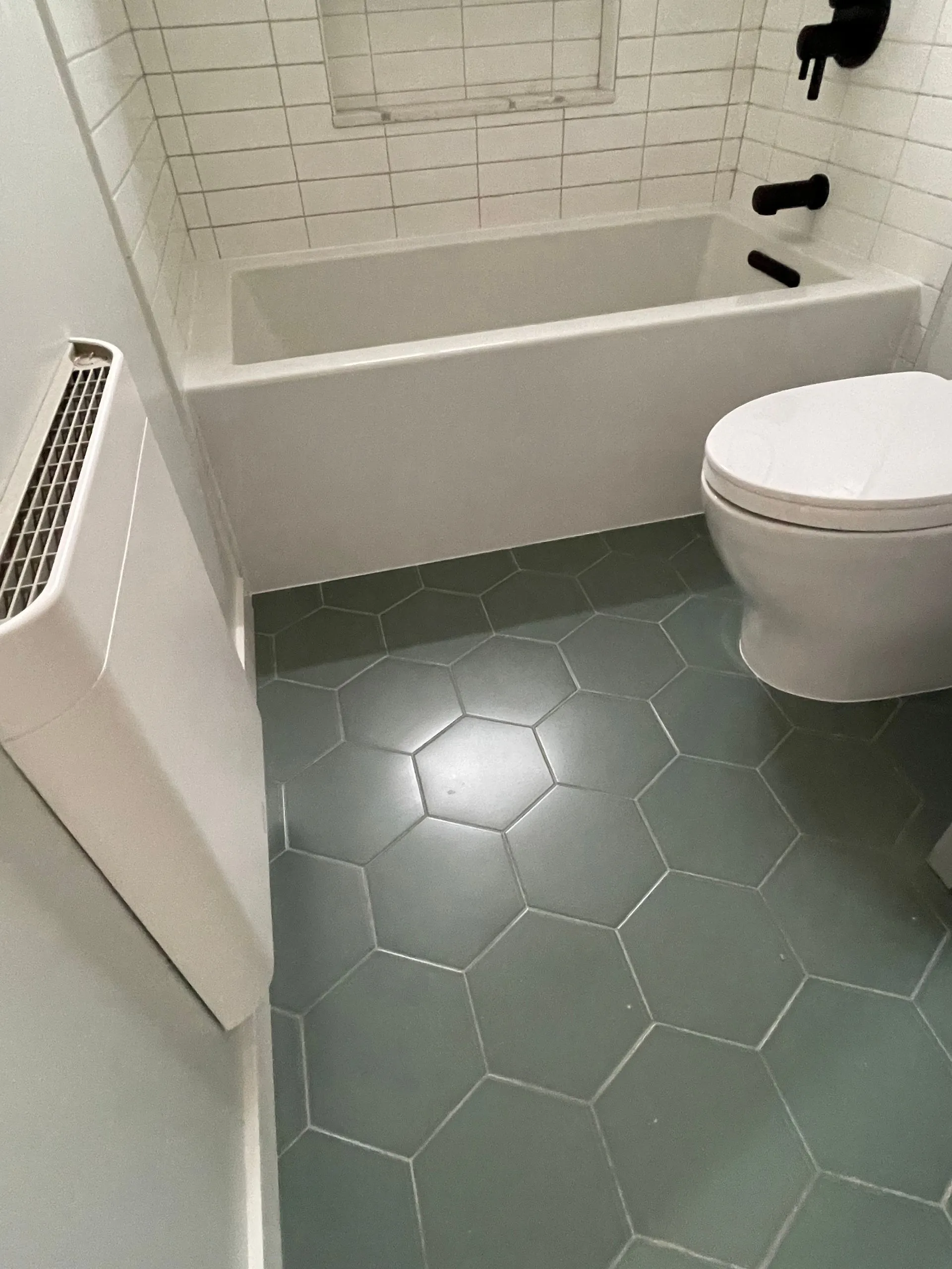 Small bathroom with white tub and toilet, green hex tile floor, and wall radiator.