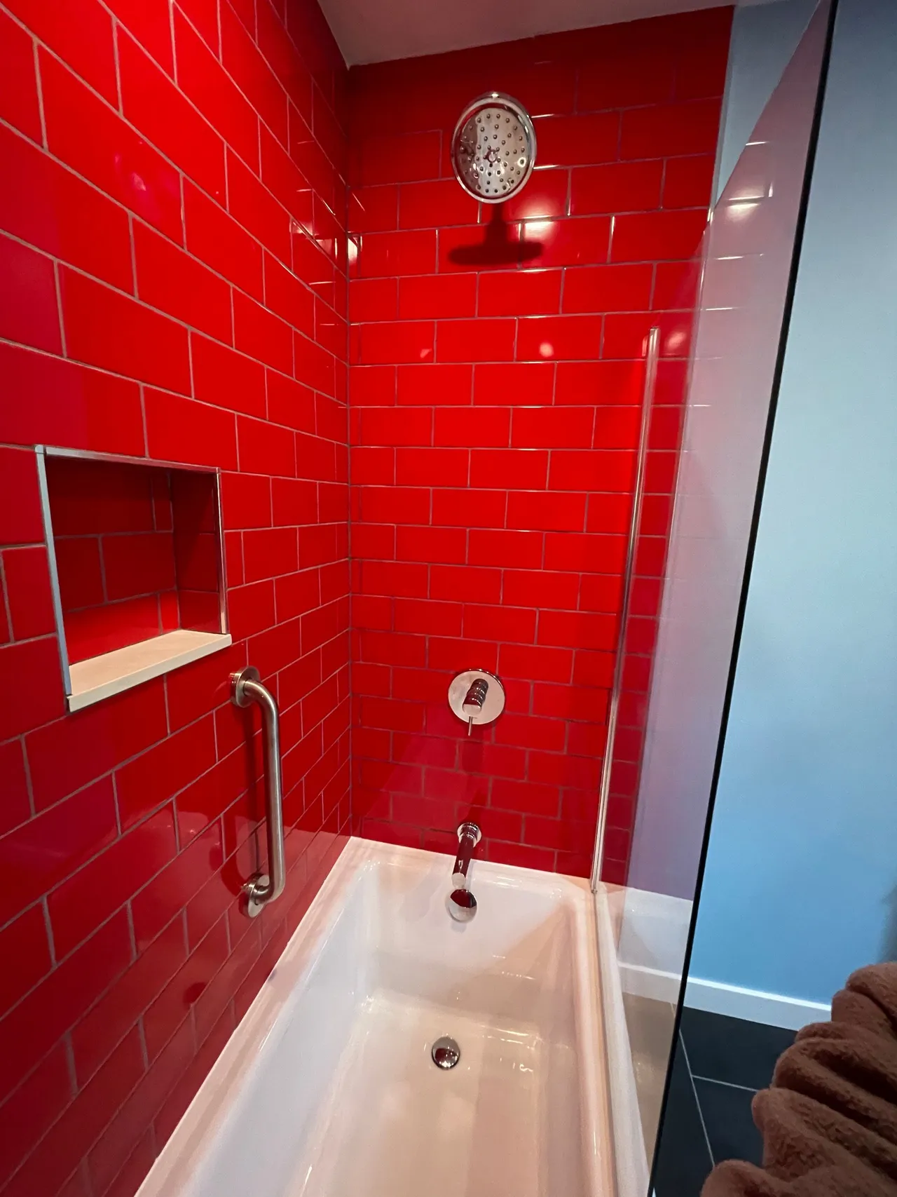 Red-tiled shower-tub with chrome fixtures and frosted glass door in a bathroom