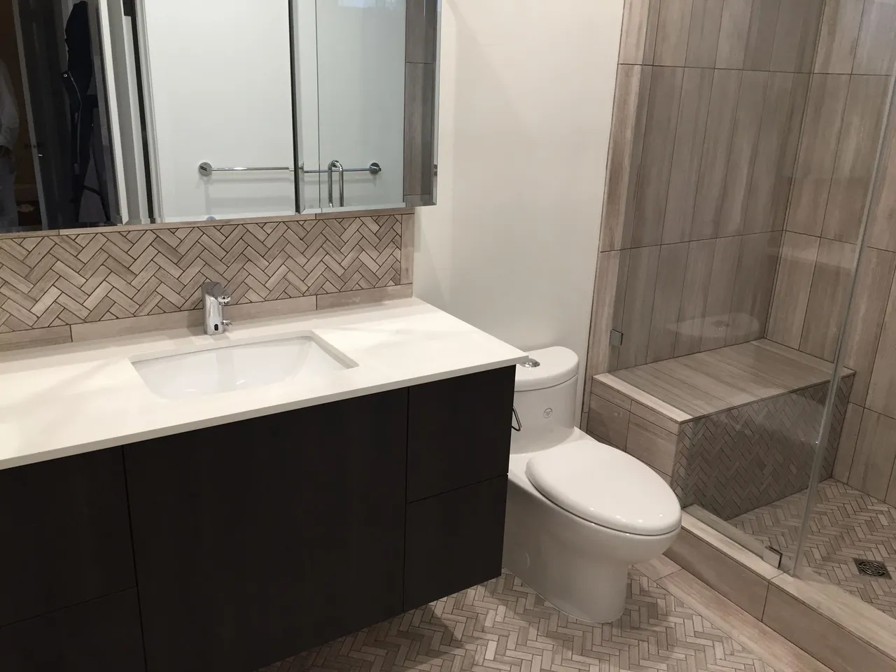 Modern bathroom with double-sink vanity, mirror, toilet, and tiled walk-in shower with bench.