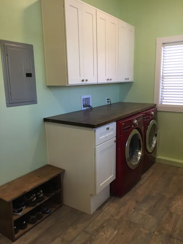 Laundry room with stacked washer and dryer, white cabinets, and a dark countertop on mint green walls.