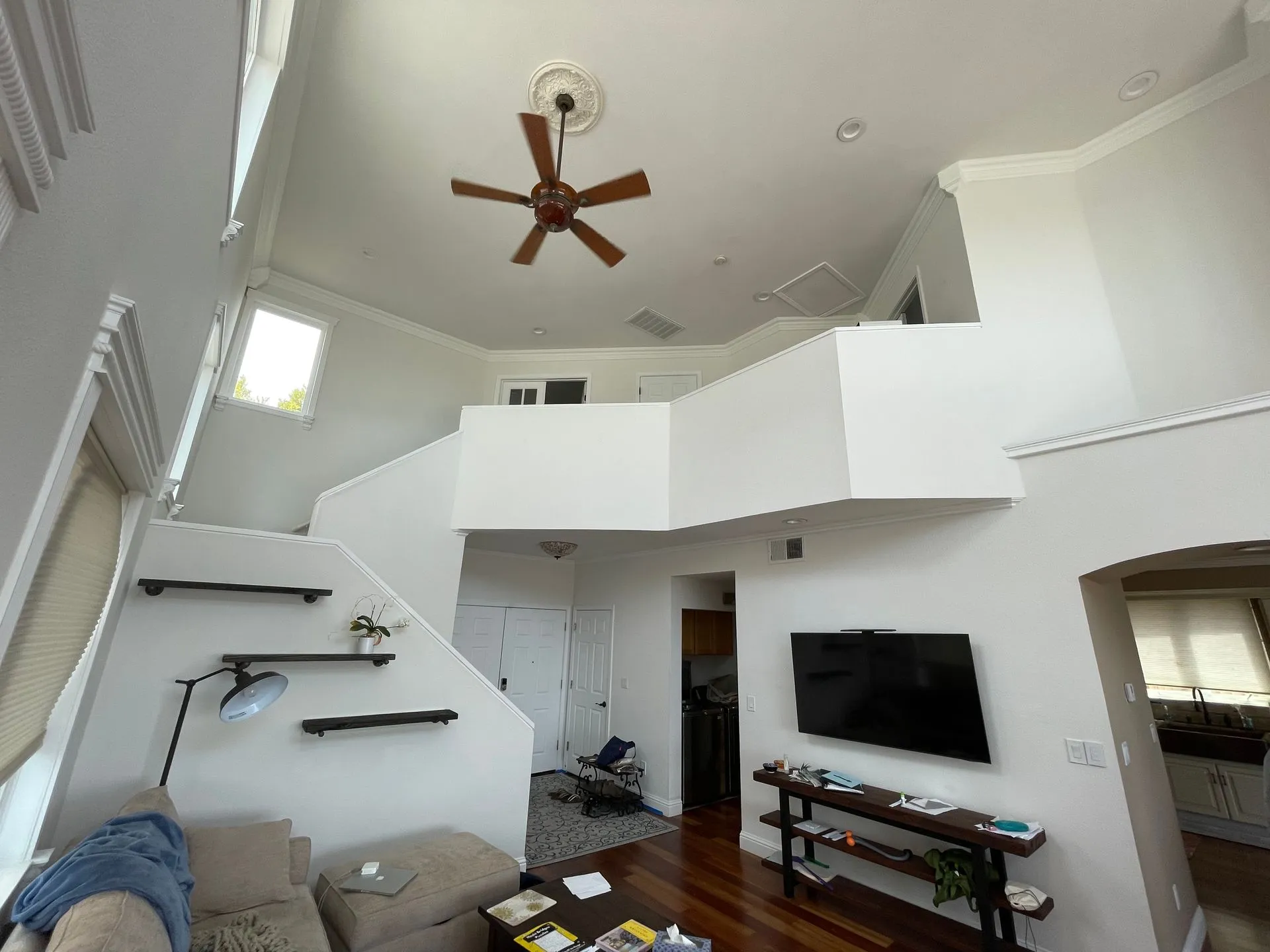Modern living room with high ceiling, ceiling fan, wall-mounted TV, staircase, and loft area