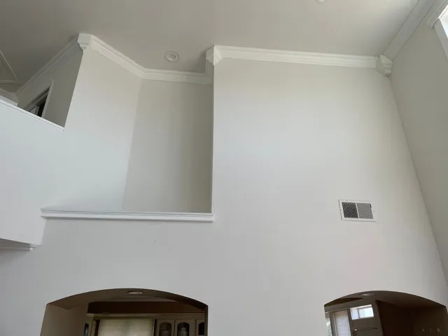 Interior with high white walls, crown molding, and two arched doorways below a small vent.