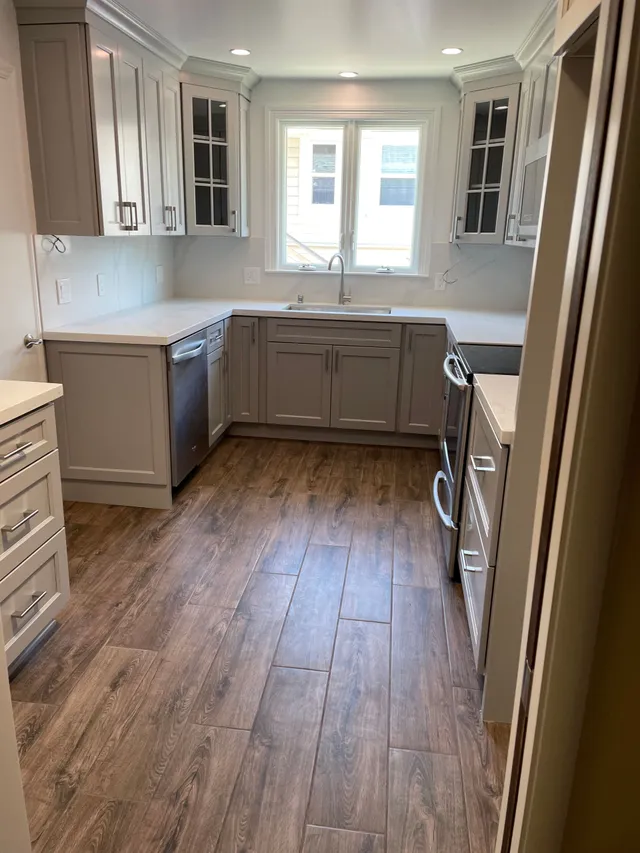 Bright remodeled kitchen with gray cabinets, wood floor, and a window over the sink