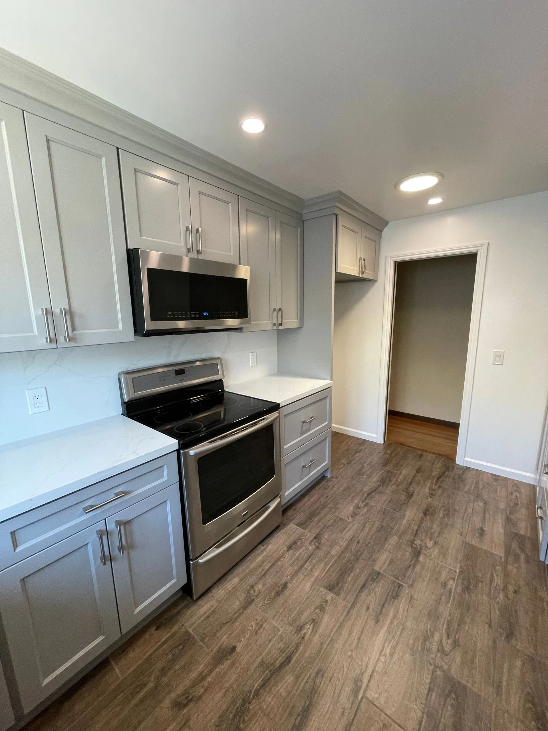 Modern kitchen with gray cabinets, stainless steel appliances, white countertops, and wood-look flooring