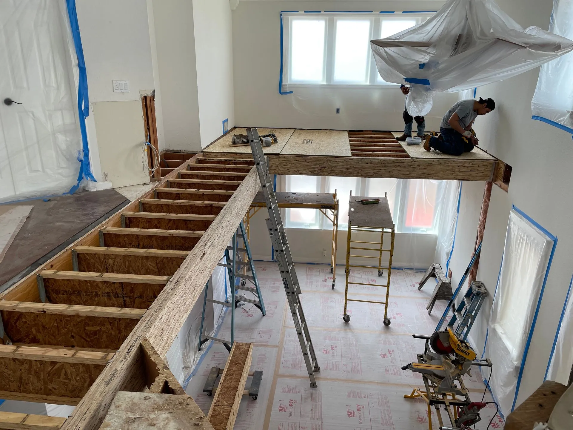 Indoor construction site with workers building a lofted mezzanine and ladder in a high-ceiling room