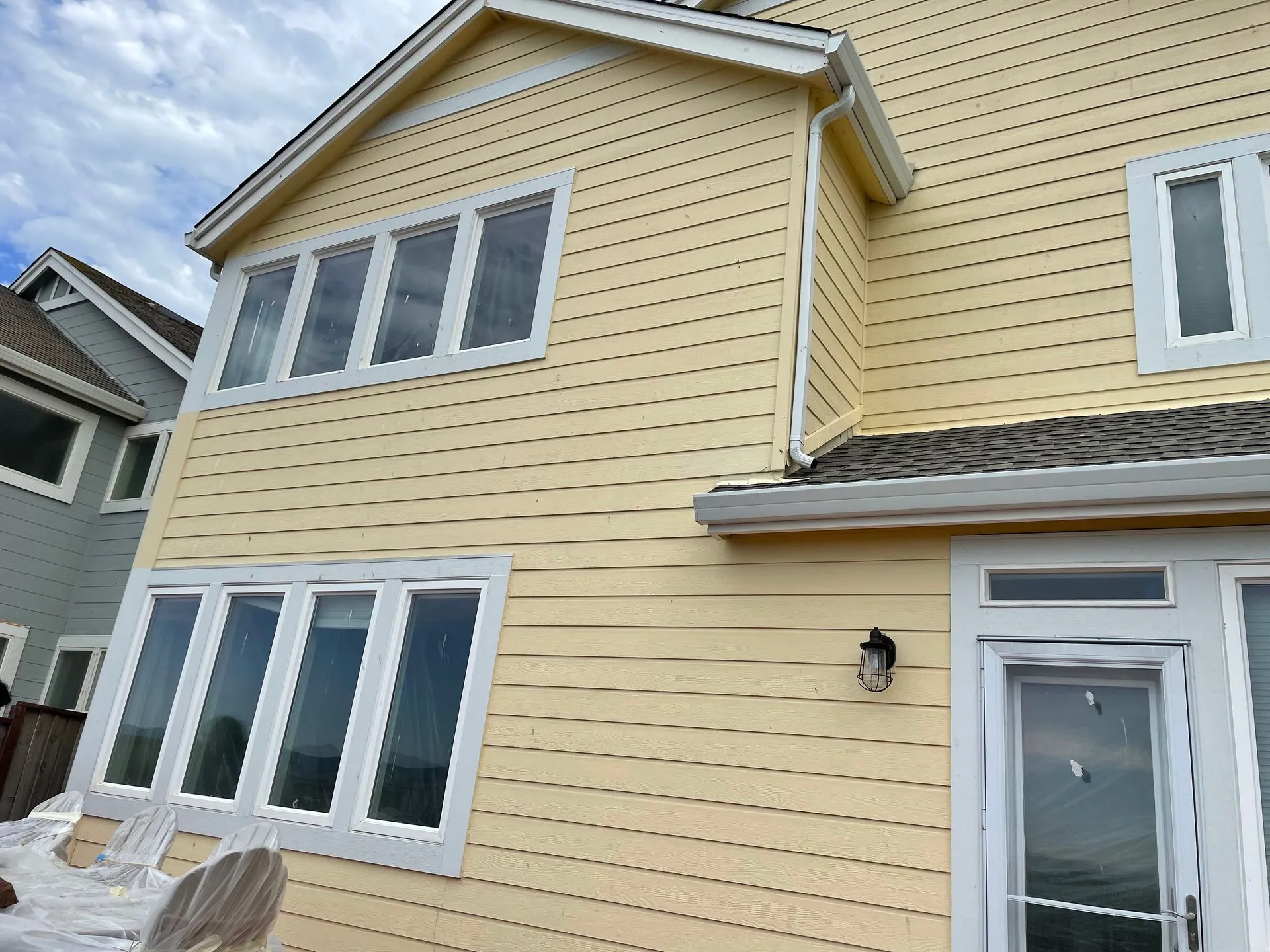 Yellow two-story house exterior with white-trimmed windows and a gray roof, viewed from below