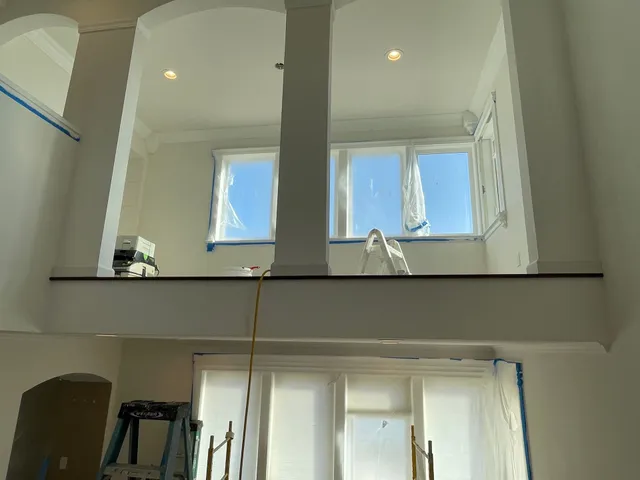 Interior view of a bright house atrium with high windows and a loft balcony above a lower room