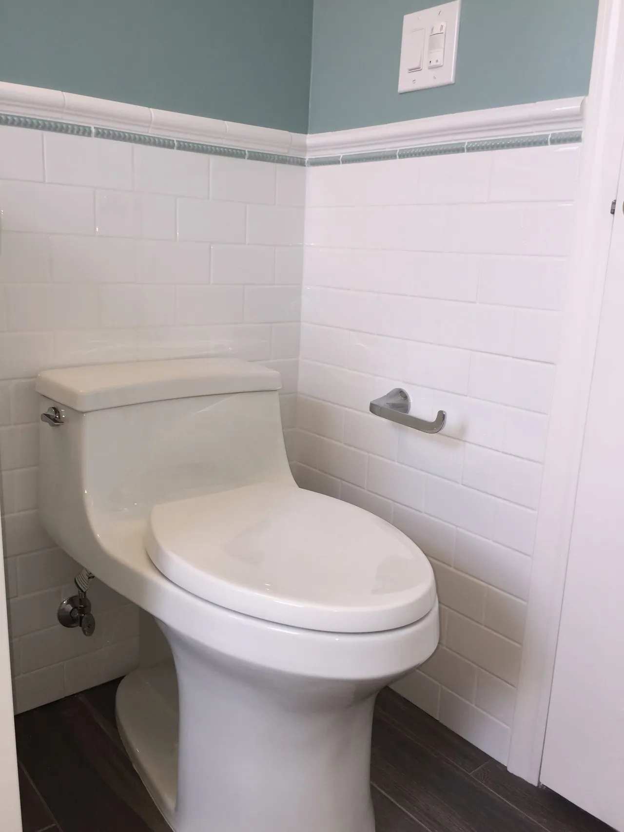 Accessible bathroom with a white toilet beside white tiled walls and a wall-mounted toilet paper holder.