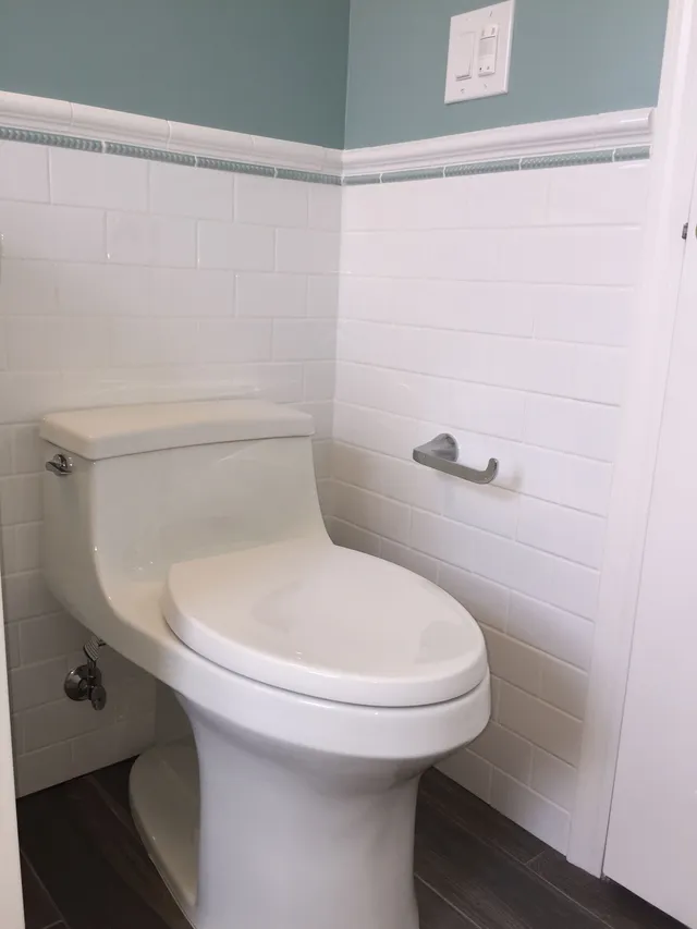 Accessible bathroom with a white toilet beside white tiled walls and a wall-mounted toilet paper holder.