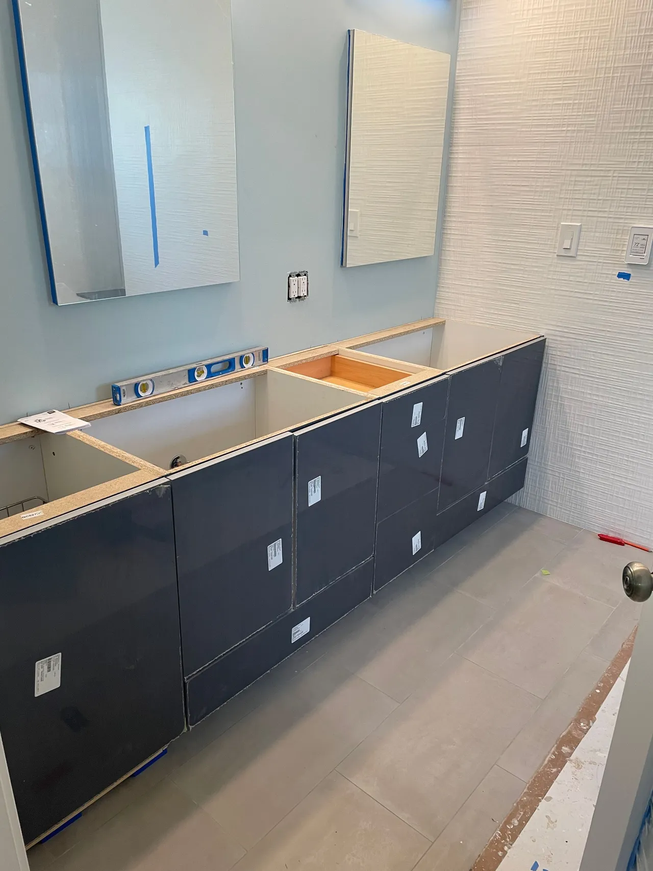 Bathroom under construction with dark cabinets, sink cutouts, and mirrors mounted on a white wall.