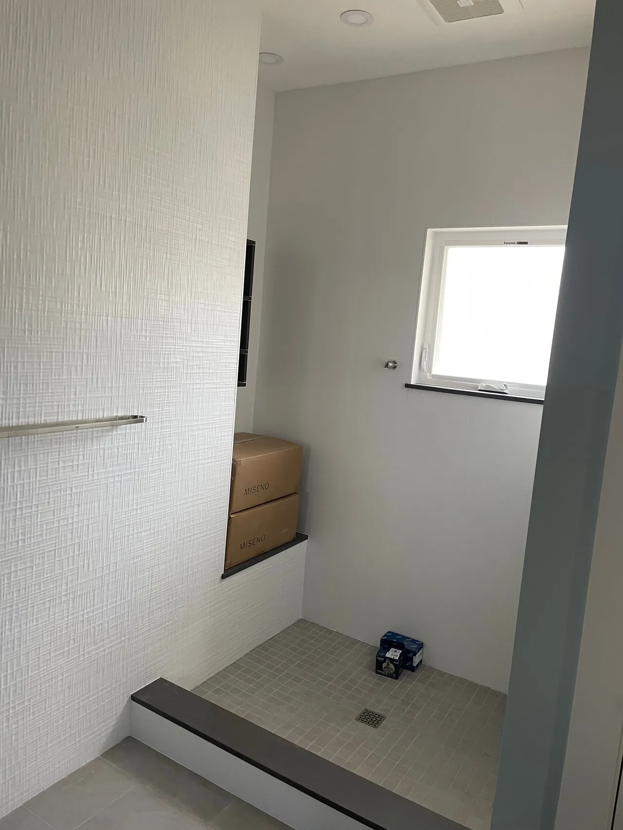Small tiled bathroom with a shower area, white walls, a window, and a wooden vanity cabinet.