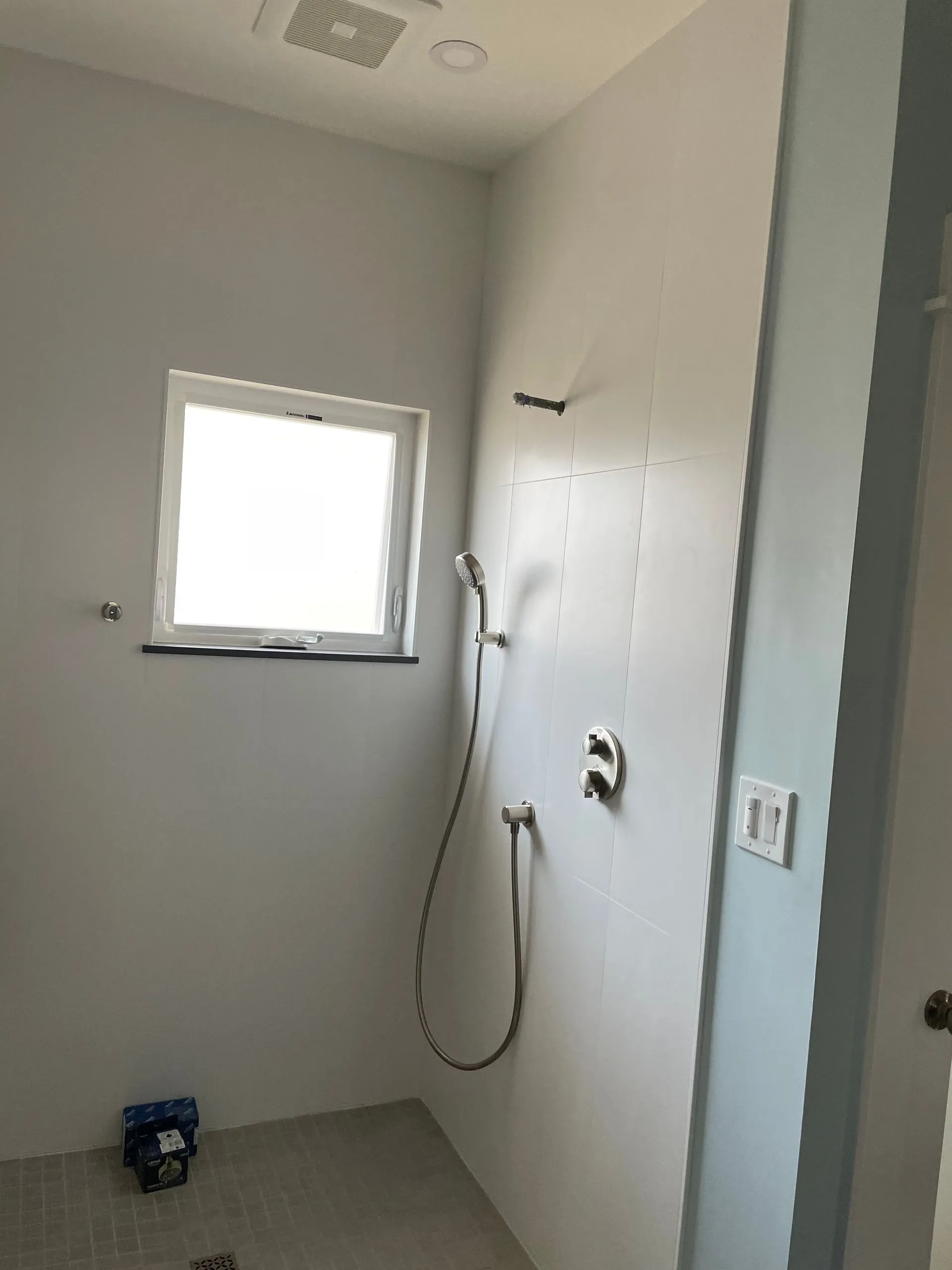 Small white tiled shower room with a window, handheld shower, and a soap dispenser on the wall.