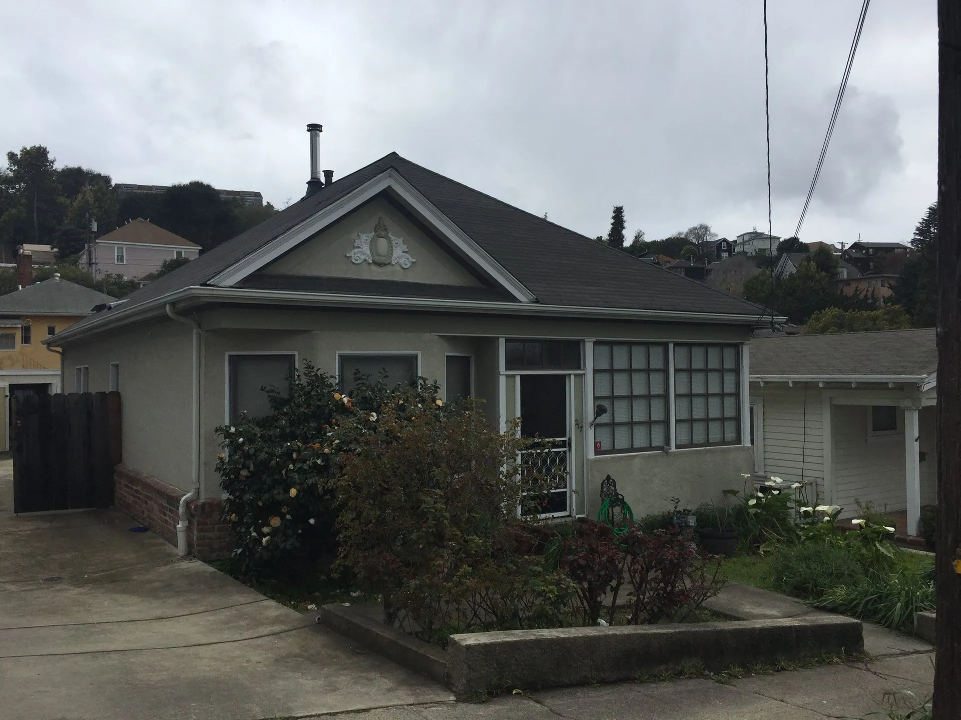 Single-story gray house with driveway, front garden, and cloudy sky.