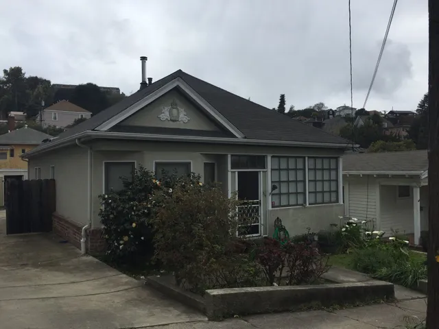 Single-story gray house with driveway, front garden, and cloudy sky.
