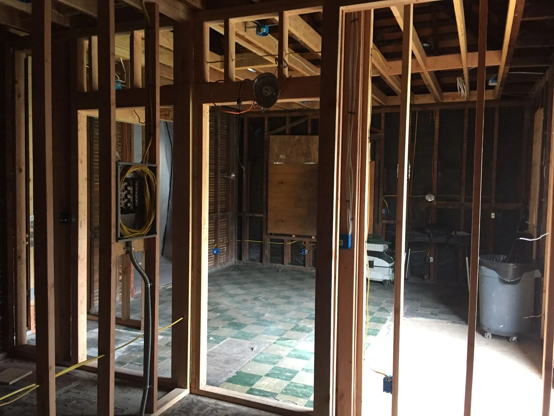 Unfinished interior with exposed wooden framing, wiring, and a checkered floor in a dim room.